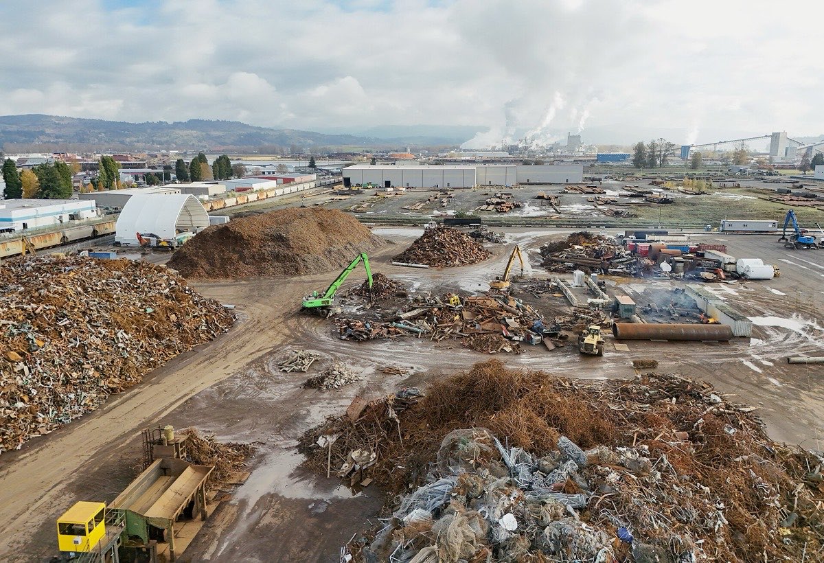 Scrap metal recycling yard with material handler sorting ferrous and non-ferrous piles
